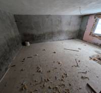 Corner room in a family house with a concrete floor and uneven walls.
