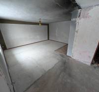 Empty room with white walls in a family house. The floor is concrete with a small section of wooden decor.