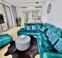 Living room of a 3-room apartment with a turquoise sofa, wooden decor flooring, and a kitchen.