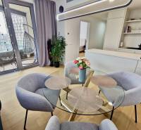 Interior of a 3-room apartment with wood-patterned flooring, a glass table, and a balcony.