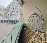 Balcony of a 3-room apartment with a wooden decor floor, a hanging chair, and a view of apartment buildings.
