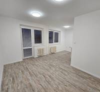 An office with white walls and a wooden decor floor, with a window and a radiator.
