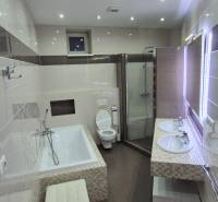 A bathroom in a family house with sinks, a bathtub, a shower, and a lighted mirror.