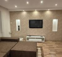 Living room in a family house with a wooden decor floor and a television on a stone wall.