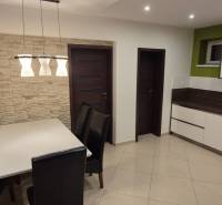 Dining room in a family house with a white table, dark chairs, and stone cladding.