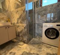 A bathroom with a washing machine, shower cabin, and marble tiles in a family house.