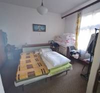 Bedroom in a family house with a colorful blanket, carpeted floor, and a picture on the wall.