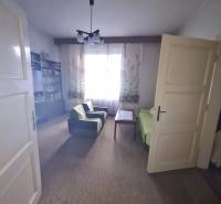 Living room in a family house with armchairs, a table, and a bookshelf, curtains letting in light.