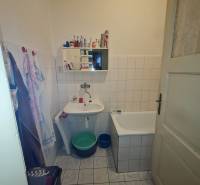 A bathroom in a family house with a bathtub, a sink, and a mirror, with tiles and white wall tiles.
