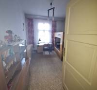 A room in a family house with a bed, a desk, a wardrobe, and decorations on the shelf.