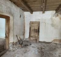 The interior of the family house with worn-out plaster and a wooden ceiling appears abandoned.