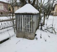 A snow-covered plot of land near a family house in Felsőtelekes with a metal shelter and trees.