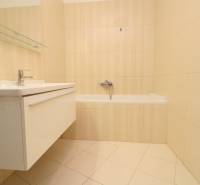Bathroom with a white bathtub and sink, beige tiles, in a two-room apartment.