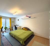 A bright bedroom in a family house with a bed, a desk, and a wooden-patterned floor.