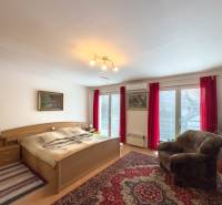Bedroom in a family house with a double bed, an armchair, and balcony doors, floor with wooden decor.