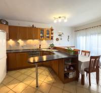 A kitchen in a family house with tiles, a dark counter, and a dining table.