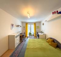 A room with a bed, a desk, a yellow curtain, and a floor with a wooden decor in a family house.