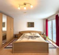 A bedroom in a family house with a wood-patterned floor, a large wardrobe, and balcony doors.