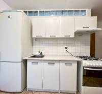 A kitchen with white cabinets and a refrigerator in a studio apartment.