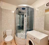 Bathroom in a studio apartment with a corner shower, washing machine, and toilet.