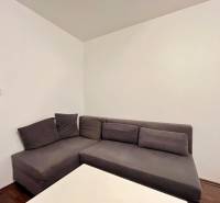 Gray corner sofa with cushions next to a white table in a studio apartment.