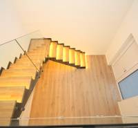 Glass staircase with backlighting and wood-patterned flooring in a family house.