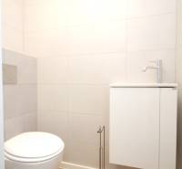 A toilet in a family house with a wooden decor floor and white walls.
