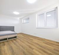 A simply furnished room in a family house with a bed and a wooden decor floor.