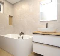 A bathroom in a family house with a bathtub, a sink, a mirror, and a floor with a wooden decor.