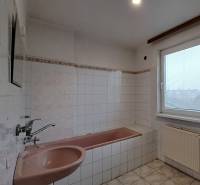 A bathroom with a bathtub and a sink in a family house with tiles and a window with a blind.