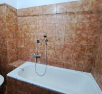 Bathroom in a family house, tiled with brown tiles, with a bathtub and a toilet.