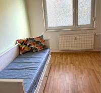 A room in a 3-room apartment with a bed, colorful pillows, and a floor with a wooden decor.