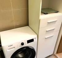 A bathroom in a 3-room apartment with a washing machine and white cabinets for storage.