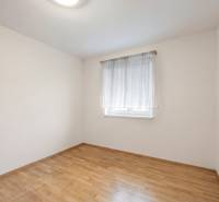 A room with a window, a white wall, and a wooden decor floor in a family house.