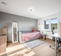 A bright room with a bed, a desk, a mirror, and a wooden floor in a family house.