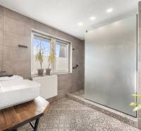 A bathroom in a family house with ceramic tiles, a sink, and a glass shower screen.
