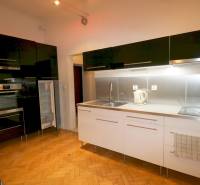 A kitchen in a 3-room apartment with a wood-patterned floor and a black kitchen unit.