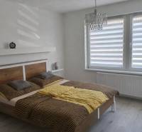Bright bedroom with a large window, bed, and wood-patterned floor in a family house.