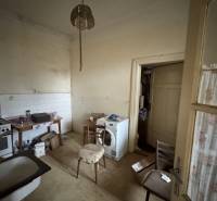 A kitchen in a family house with older furnishings, a washing machine, and wooden furniture.