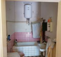 A bathroom in a family house with pink tiles and a boiler above the bathtub.