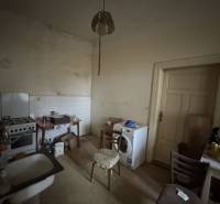 A kitchen in a family house with a sink, stove, and washing machine, with old furniture and lighting.