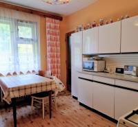 A kitchen in a family house with a wooden decor floor, white cabinets, and a checkered tablecloth.