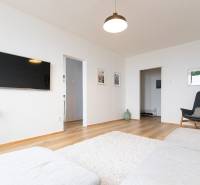 Living room in a three-room apartment with a television, sofa, and wooden decor flooring.