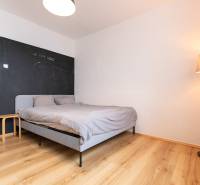 A bedroom with a bed, wood-patterned flooring, and a standing lamp in a three-room apartment.
