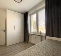 Bedroom in a 3-room apartment, wooden decor flooring, large window with curtain.