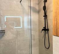 A shower enclosure with glass doors and a black showerhead in a 3-room apartment.