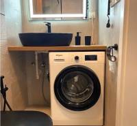 Compact bathroom with a washing machine and wooden decor flooring in a 3-room apartment.