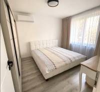 Bedroom in a 3-room apartment with a large window, bed, and wooden decor flooring.