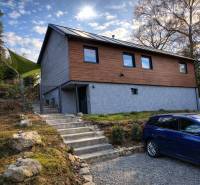 A cottage in Zvolen with wooden cladding, stairs, and a parked car on a gravel surface.