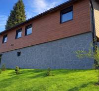 A cottage in the town of Zvolen with a stone and wooden facade surrounded by a manicured lawn.